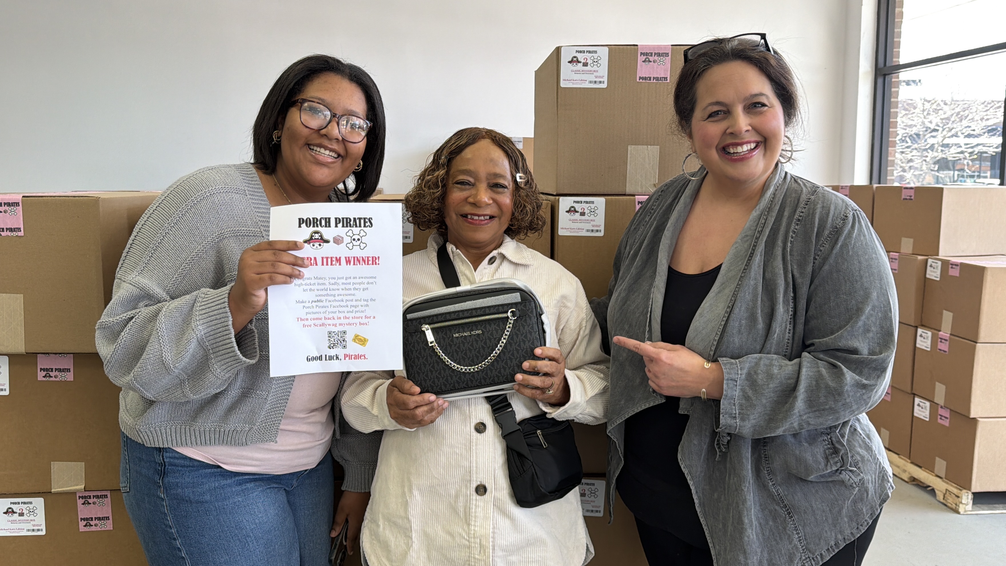Three women smiling with a Michael Kors bag and an Ultra Item Winner sign