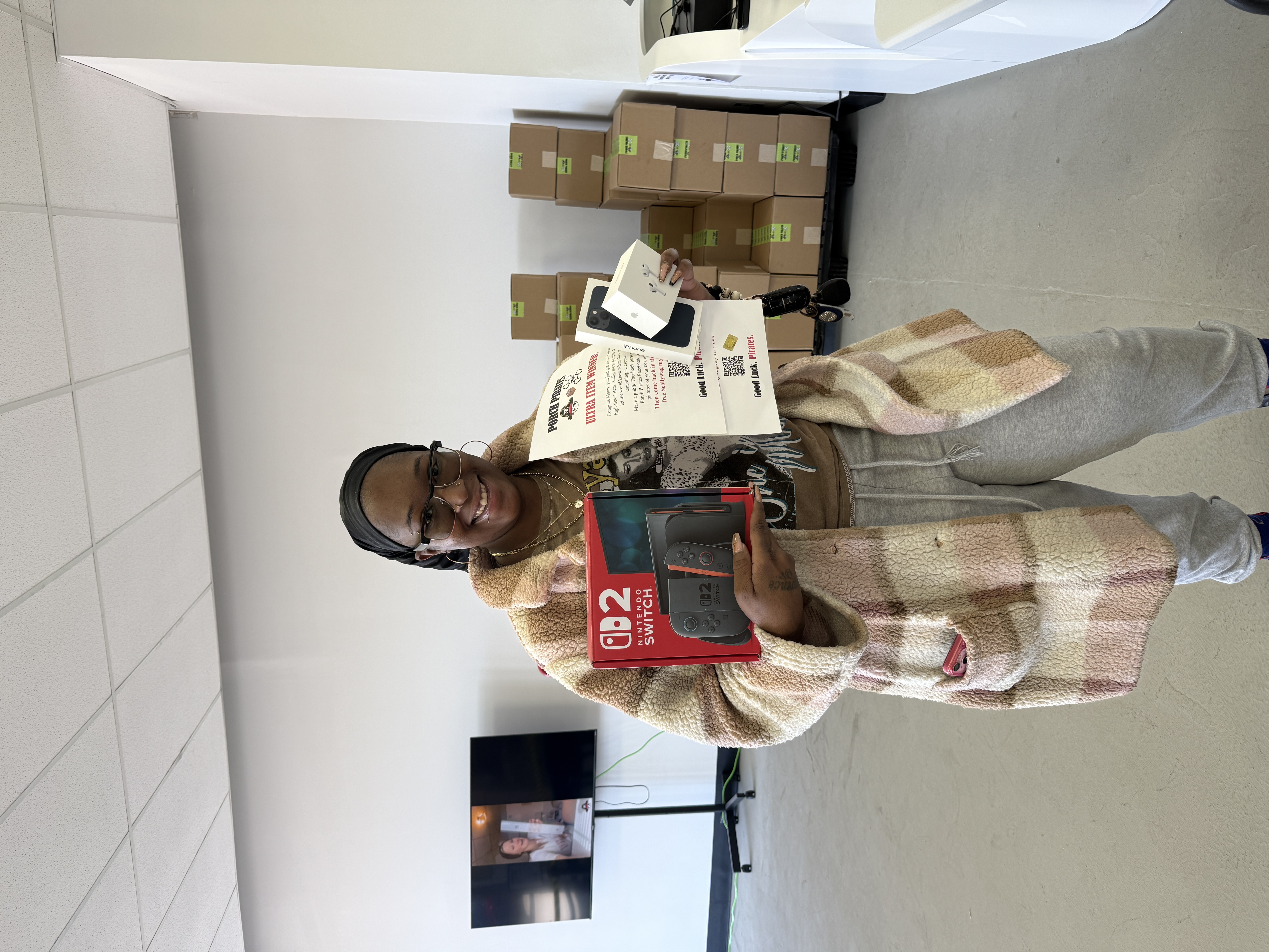 Customer holding a Switch 2, an iPhone and AirPods with a winner sign