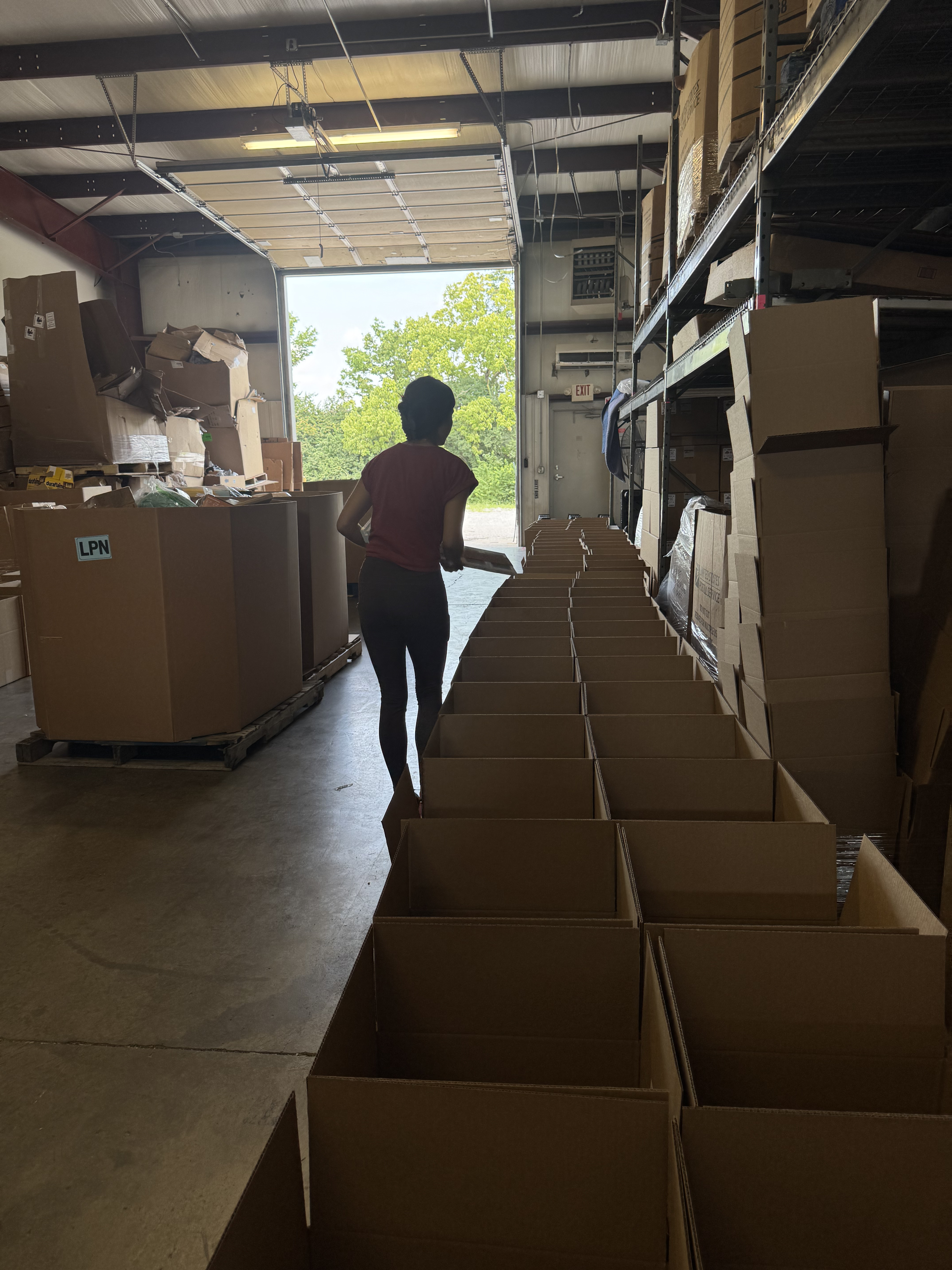 Crew member walking the packing line of open mystery boxes toward the dock door